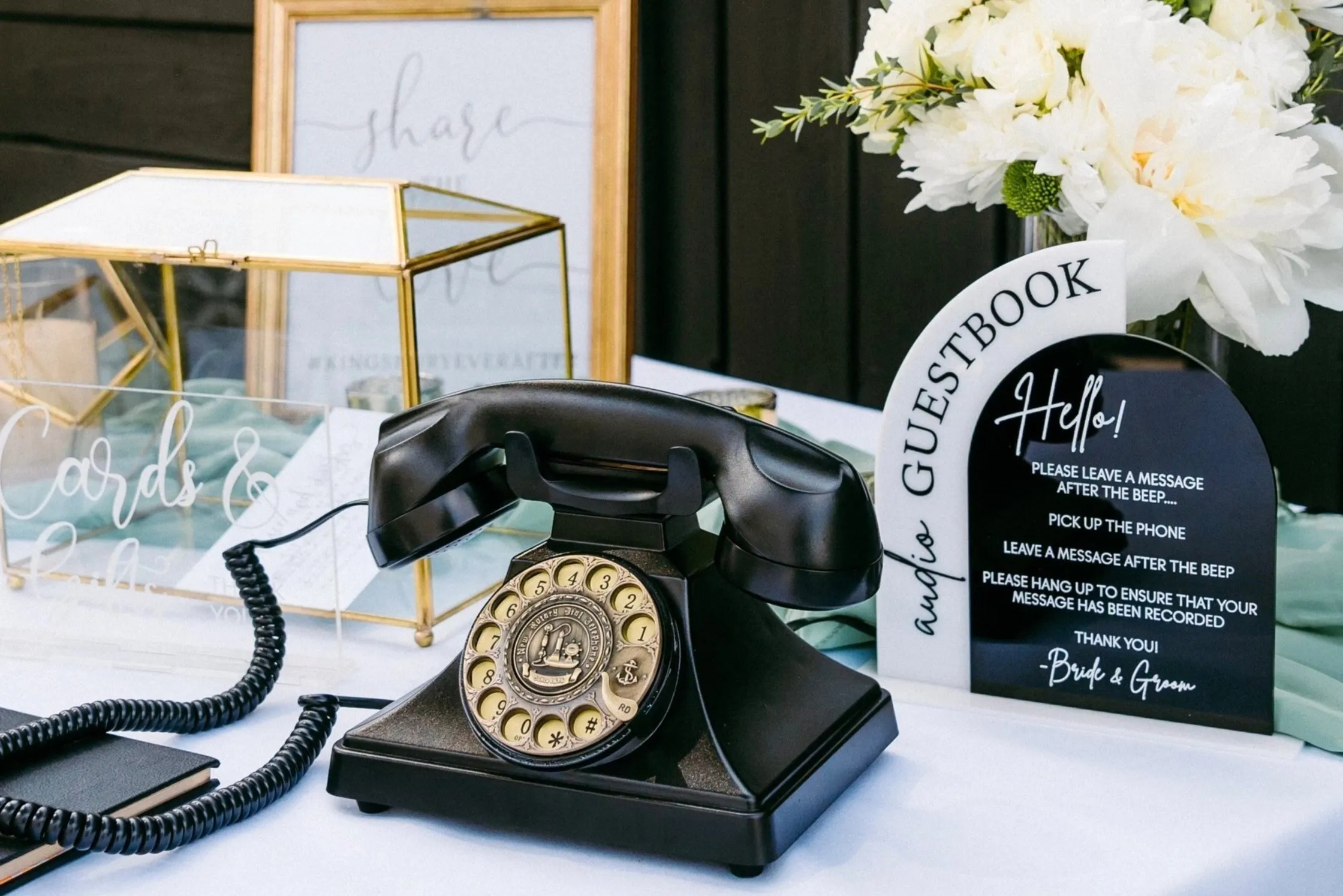 Чёрный дисковый телефон на столе рядом с табличкой Audio Guestbook и коробкой для открыток