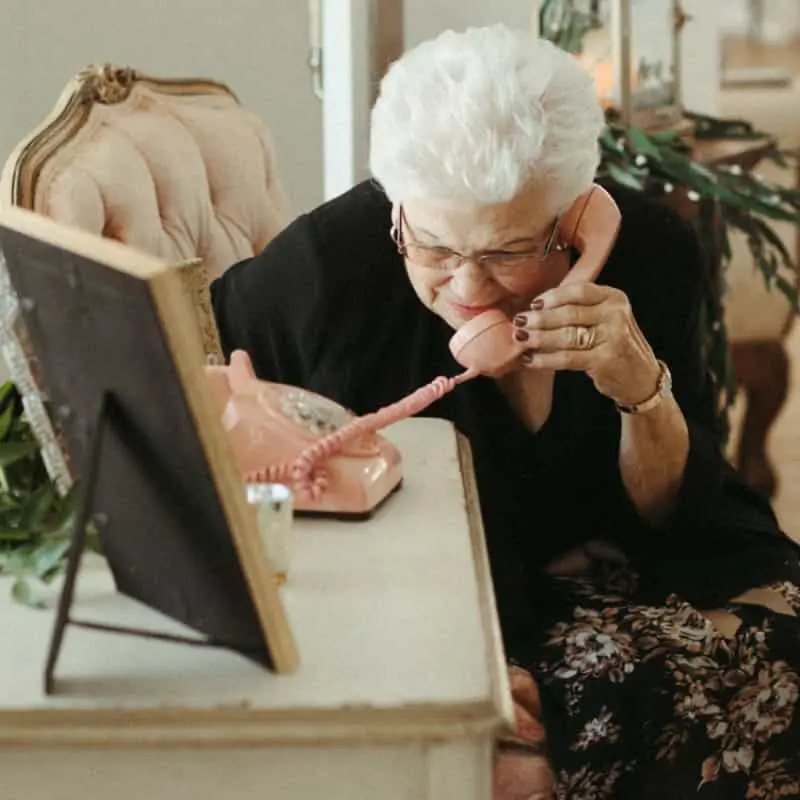 An older lady leaving a message on a pink rotary phone