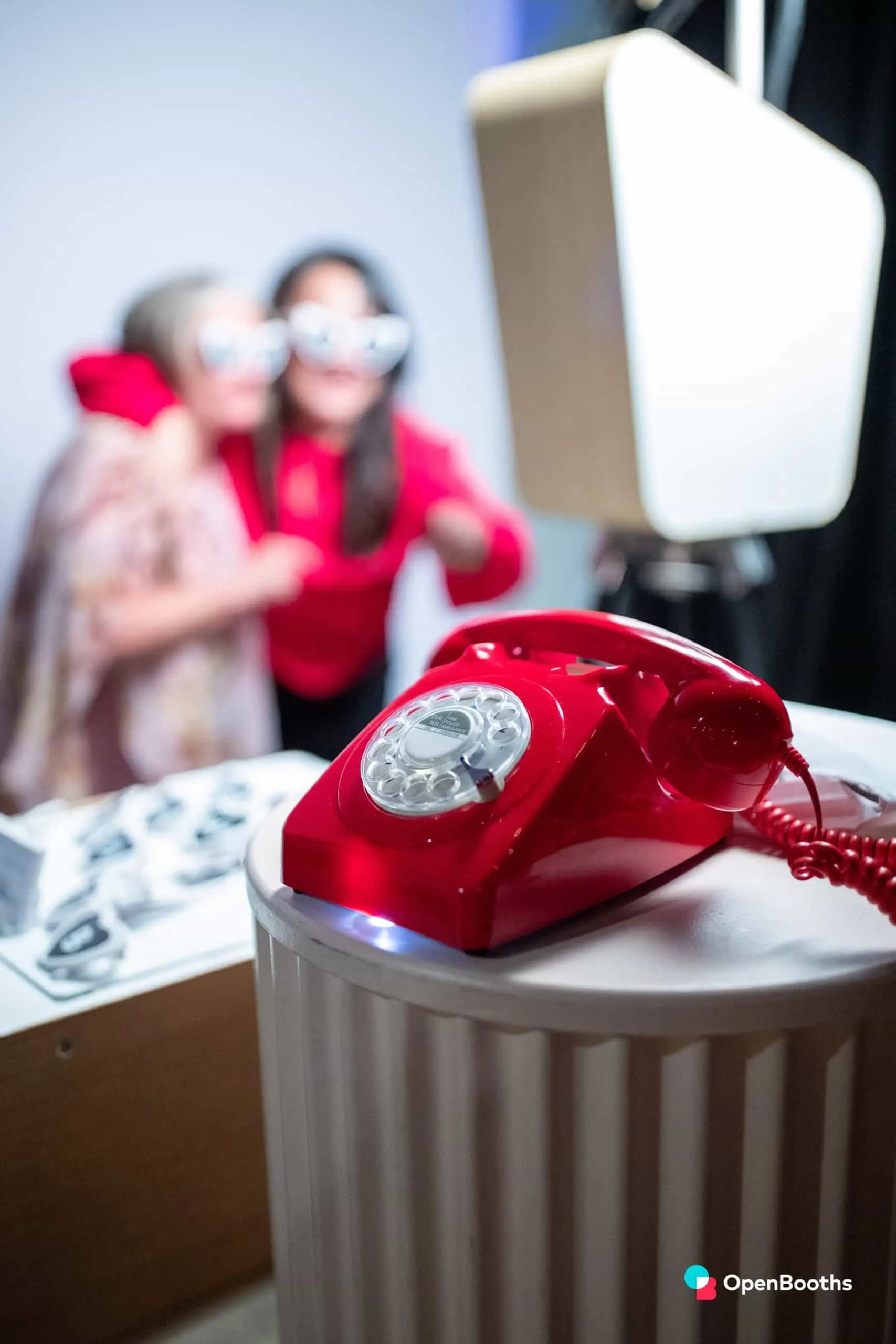 Red rotary phone on a white pedestal, with guests in the background