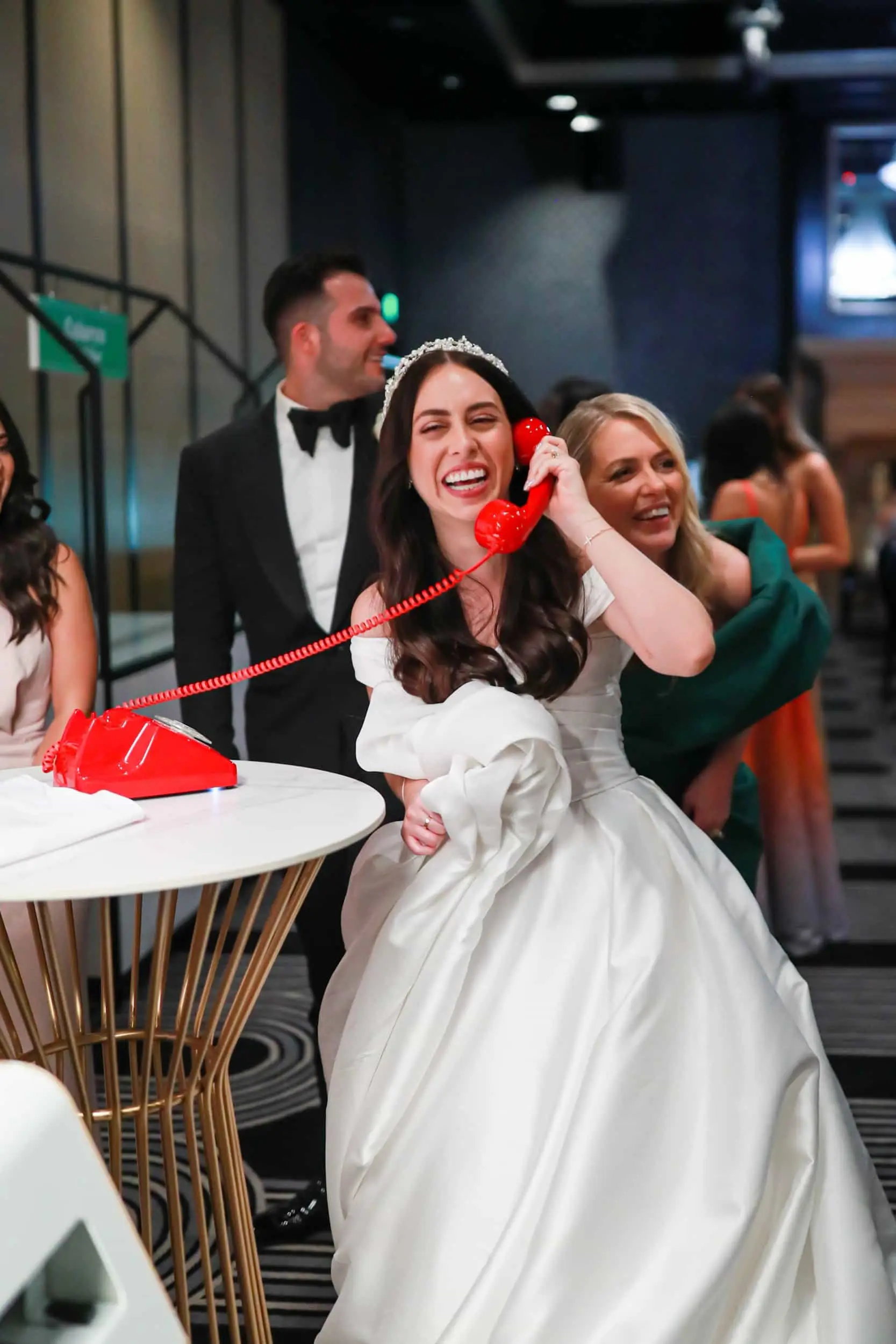 Bride laughing at the red phone, with the groom and a guest behind her