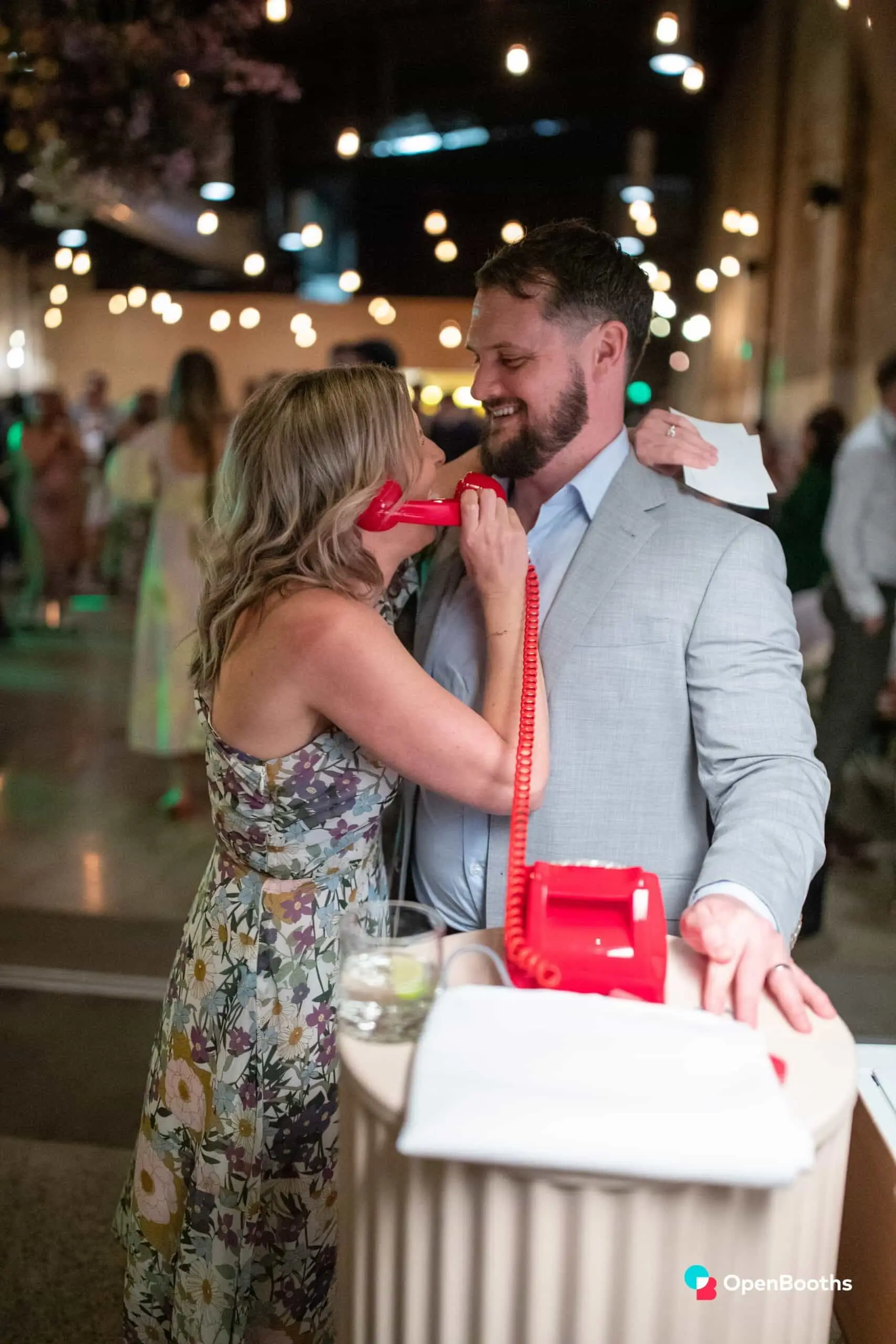 A guest speaking into the red phone, a smiling man with his arm around her neck