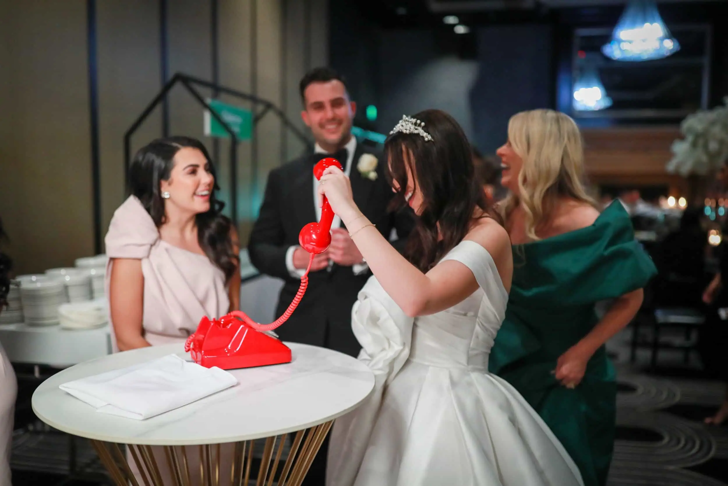 Bride leaving a message on the red phone, with guests laughing around her