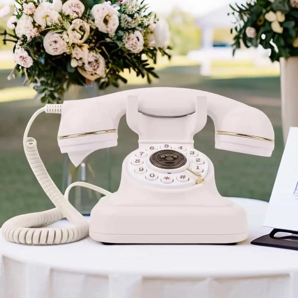 Белый ретро телефон Elegance70 White на столе под открытым небом рядом с цветами