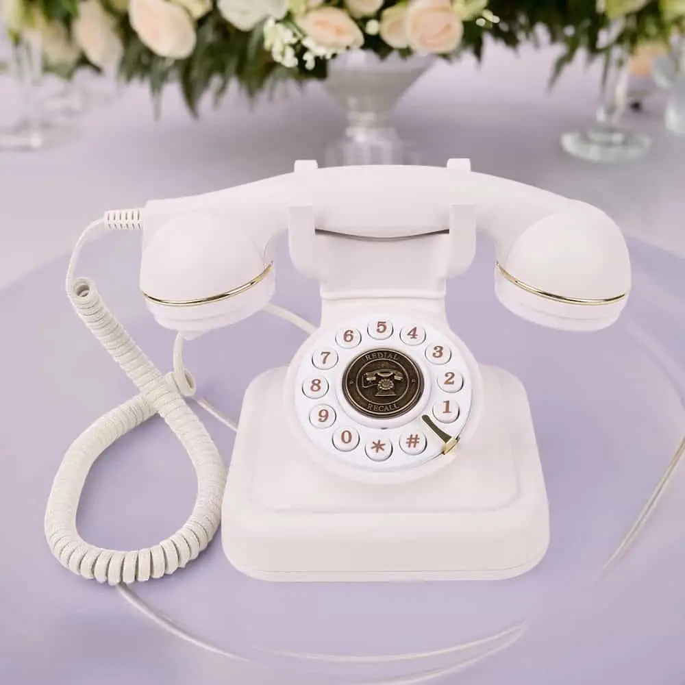Белый ретро телефон Elegance70 White на сиреневом столе под цветочными композициями